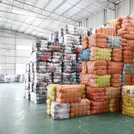 Nave llena de fardos de ropa de segunda mano prensados y embolsados en rafia naranja, verde y transparente, apilados en columnas de varios metros hasta casi el techo